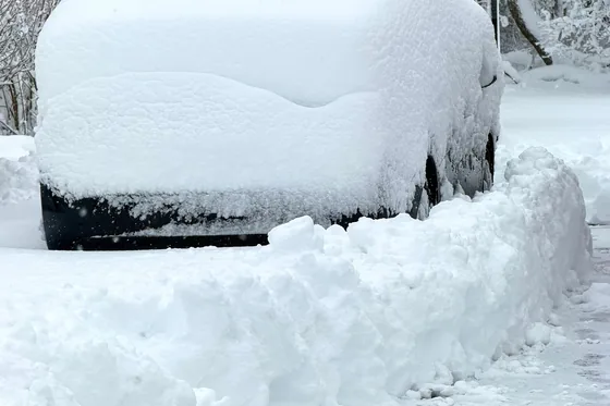 A car buried to the windows in snow beside a cleared bank