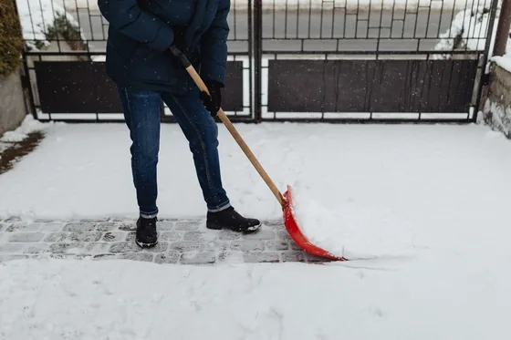 A crew member hand-shovelling a paved entrance path