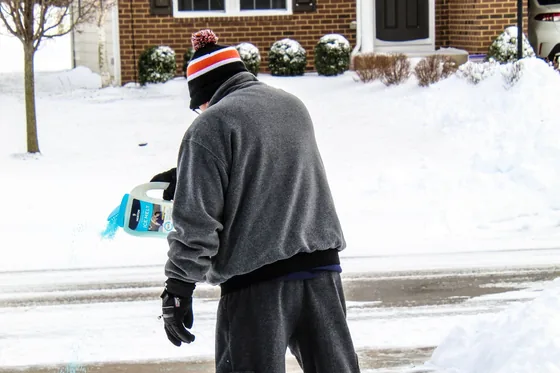A crew member applying ice melt along a cleared driveway
