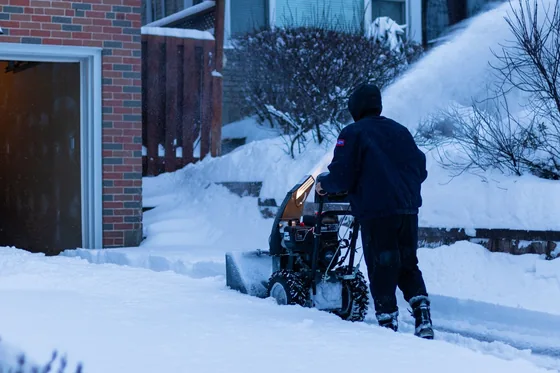 An operator clearing a residential walkway with a snow blower